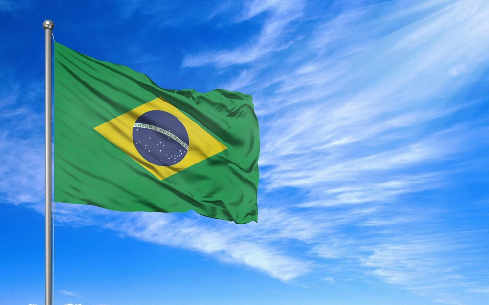 Imagem de uma bandeira do Brasil. Ao fundo, é possível notar o céu azul.