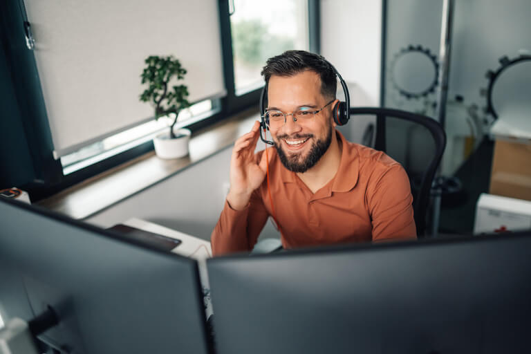 Imagem de um homem sentado em frente de um computador de duas telas. Ele está trabalhando como Correspondente Bancários e realizando vendas no fim de ano.