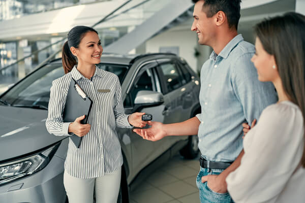Imagem de um homem e uma mulher, servidores públicos, comprando um carro com uma atendente.