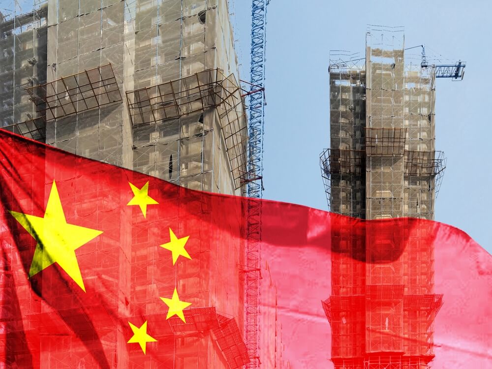 Imagem de prédios sendo construídos, inacabados, com uma bandeira da China à frente, representando a crise imobiliária que o país enfrenta.