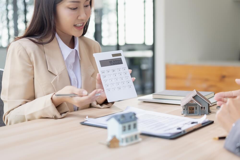 Imagem de uma mulher segurando uma calculadora e apresentando valores do financiamento imobiliário.