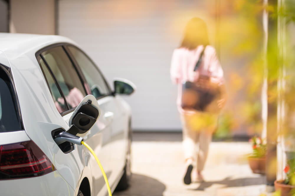 Imagem de uma carro elétrico carregando, enquanto a proprietária se distancia. 