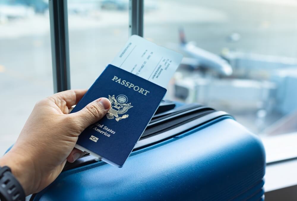 Imagem de uma mão segurando um passaporte de viagens, em um aeroporto.