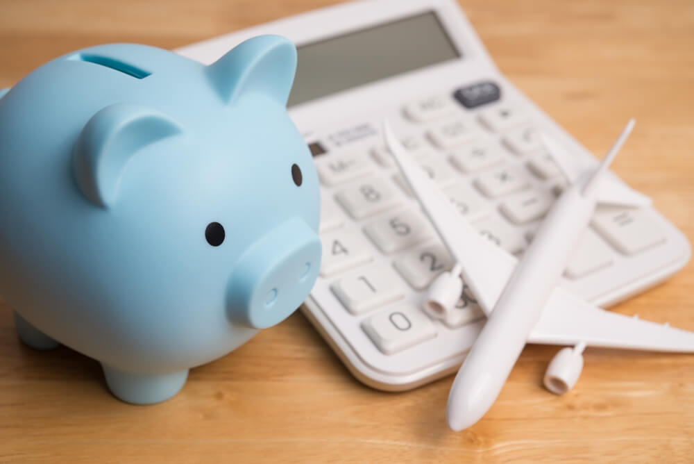Imagem de um porquinho azul, ao lado de um avião e de uma calculadora, representando o consórcio de viagens.