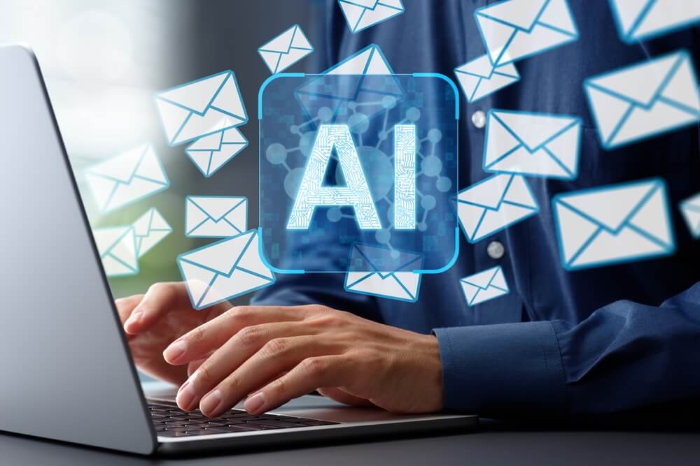 Imagem de um homem utilizando o computador. Na tela, está escrito AI, sigla para Inteligiência Artificial. Há também envelopes voando, ilustrando.