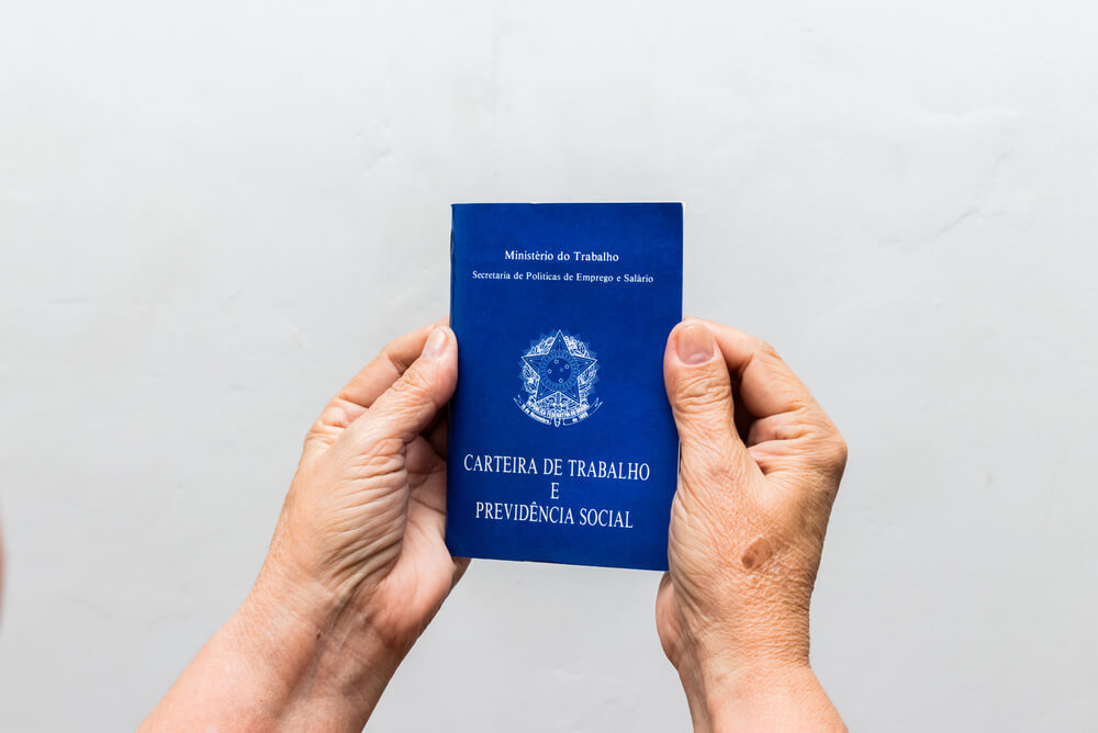 Imagem focada em duas mãos segurando uma Carteira de Trabalho.