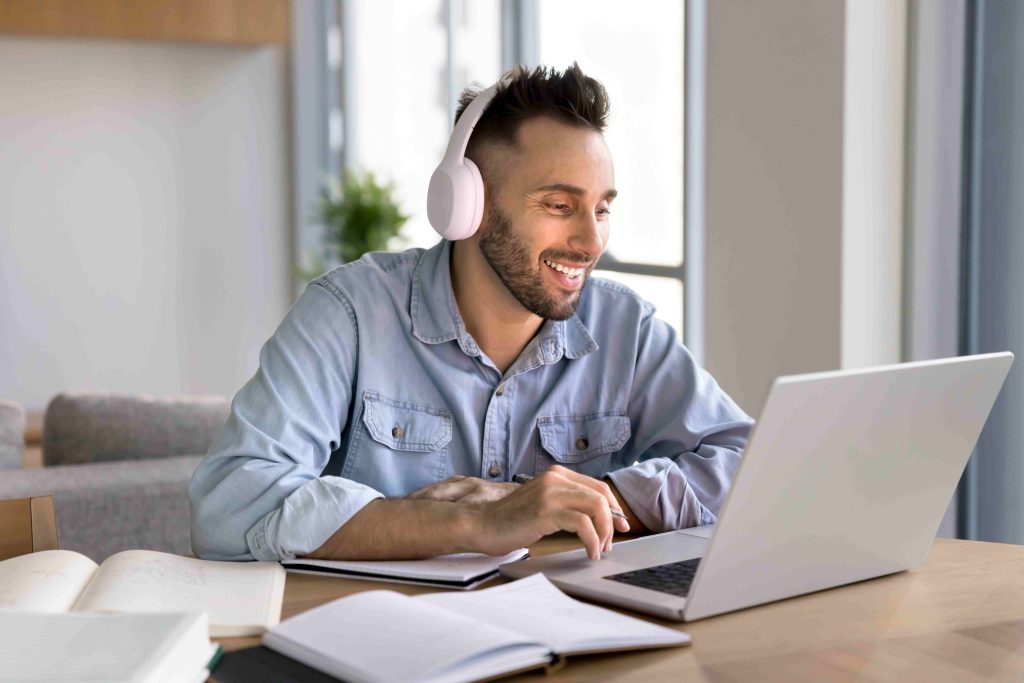 Imagem de um homem branco sentado em uma mesa de computador. Ele está estudando e tirando o certificado pldft.