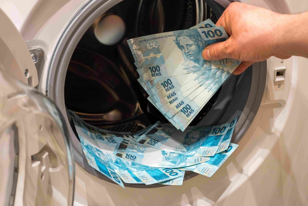 Imagem de dinheiro sendo colocado dentro da máquina de lavar, representando o crime de lavagem de dinheiro.