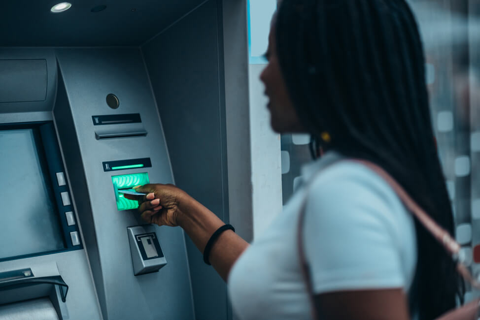 Imagem de uma mulher negra realizando um saque em um caixa eletrônico.