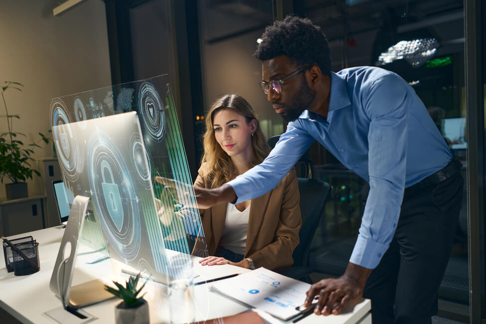 Imagem de um homem negro explicando algo na tela de um computador para uma mulher branca. Eles trabalham em uma fintech.