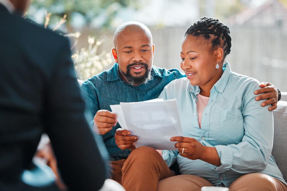 Imagem de um casal, um homem e uma mulher, ambos negros, contratando um seguro com uma corretora de seguros.