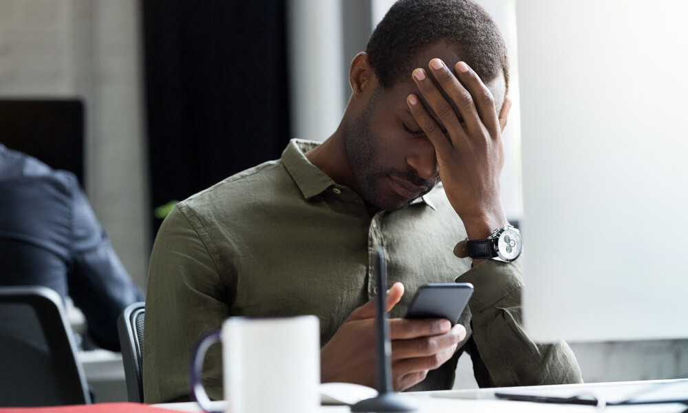 Imagem de um homem. Ele está com a mão na cabeça e segurando um celular, após ter perdido o fechamento de um contrato com um cliente.