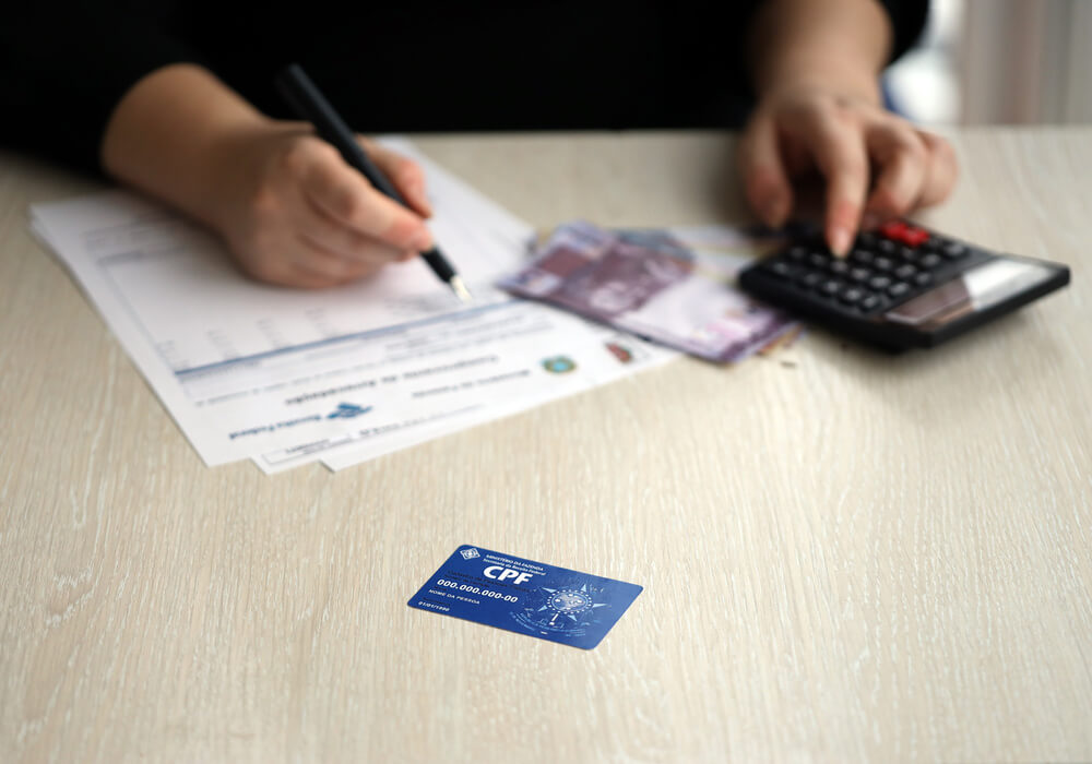 Imagem de uma pessoa fazendo contas em uma calculadora. Ela está com o CPF perto.