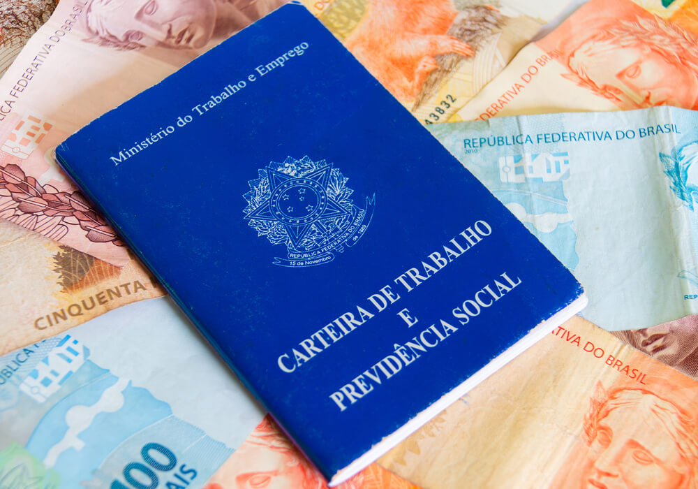 Imagem de um Carteira de Trabalho em cima de uma série de notas de dinheiro.