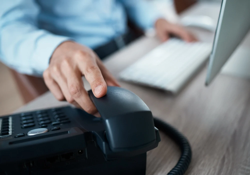Imagem da mão de um homem pegando no telefone. Ele irá fazer uma ligação utilizando uma discadora para consignado.