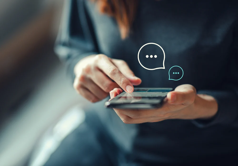 Imagem de uma mulher utilizando o celular. Ela está vendo um SMS de consignado que recebeu.